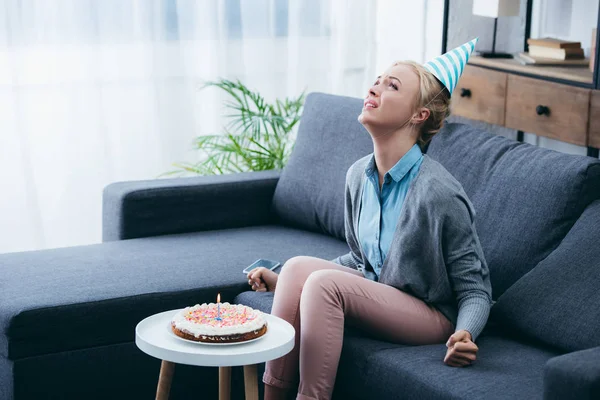Frustrierte Frau mit Partyhut feiert Geburtstag allein zu Hause — Stockfoto