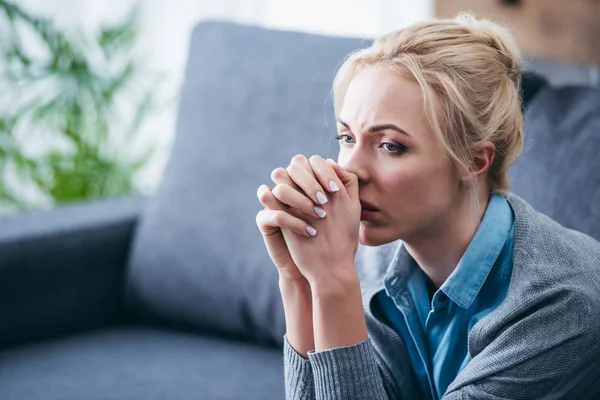 Selektiver Fokus einer aufgebrachten Frau mit gefalteten Händen, die zu Hause sitzt — Stockfoto