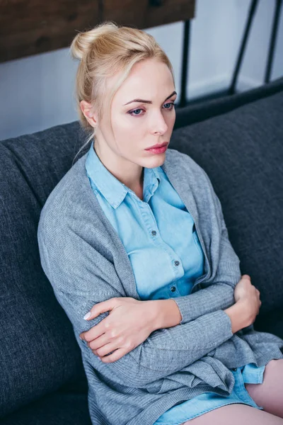 Красива засмучена жінка з схрещеними руками сидить на дивані вдома — стокове фото