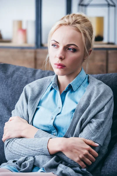 Selective focus of beautiful upset woman with arms crossed sitting on couch at home — Stock Photo