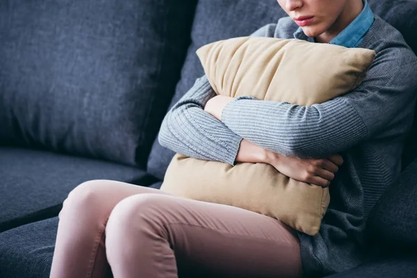 Cropped view of woman sitting on couch and holding pillow at home — Stock Photo