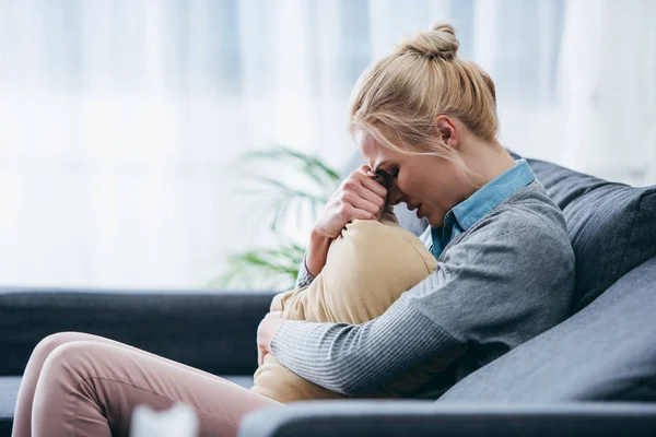 Traurige Frau sitzt auf Couch, weint und hält Kissen zu Hause — Stockfoto