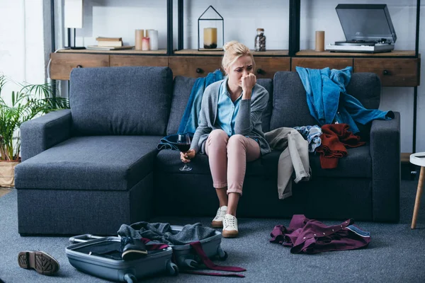 Femme déprimée assise avec un verre de vin rouge et pleurant pendant l'emballage dans le salon après avoir rompu avec son petit ami — Photo de stock