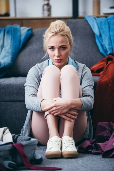 Sad woman sitting with scattered clothes after breaking up with boyfriend and looking at camera — Stock Photo