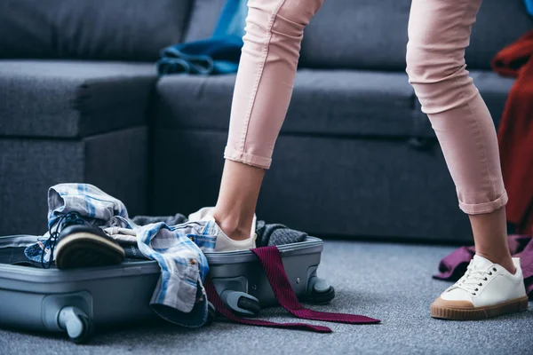 Vista recortada de la mujer empujando la ropa en la maleta con la pierna después de romper con el novio — Stock Photo