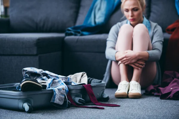 Donna triste seduta con vestiti sparsi e valigia dopo aver rotto con il fidanzato — Foto stock