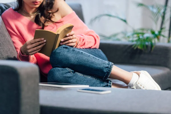 Vista recortada de la estudiante sentada en el sofá y libro de lectura - foto de stock