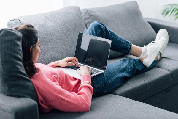 Indianerin benutzt Laptop mit leerem Bildschirm im Liegen auf Sofa — Stockfoto