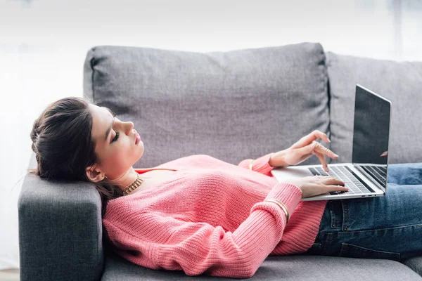 Indianerin benutzt Laptop mit leerem Bildschirm im Liegen auf Sofa — Stockfoto