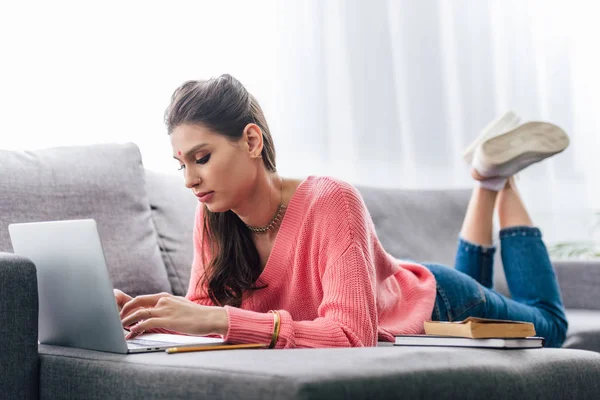 Beautiful indian woman with bindi studying with books and laptop on sofa — Stock Photo