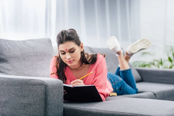 Female indian student with bindi writing in notebook on sofa — Stock Photo