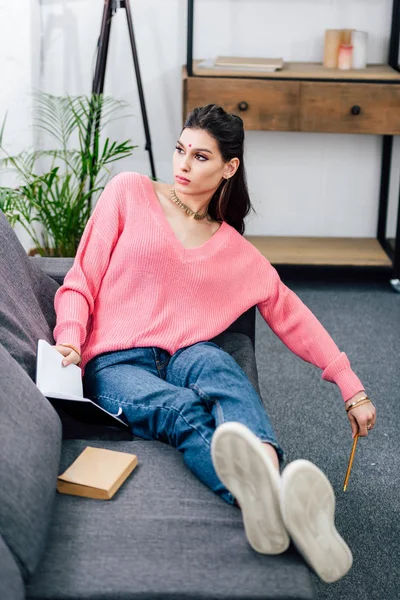 Beautiful indian student studying with book and notebook on sofa — Stock Photo