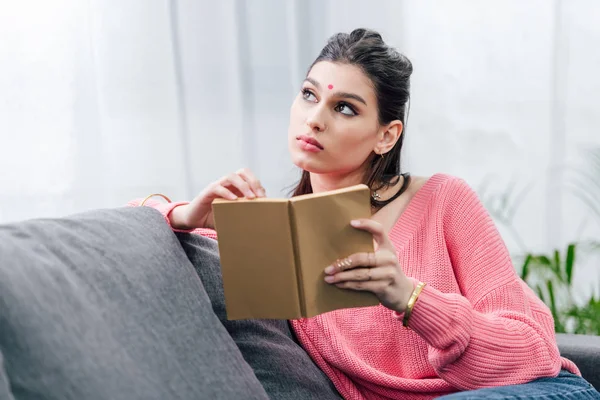 Estudante indiano do sexo feminino ler livro e pensar no sofá — Fotografia de Stock