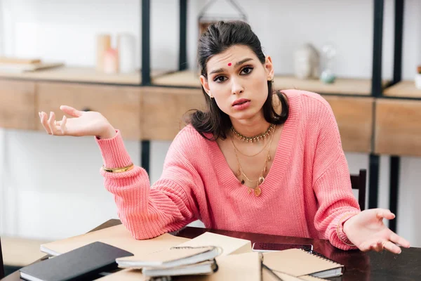 Sad indian student with bindi studying with notebooks and showing shrug gesture at home — Stock Photo