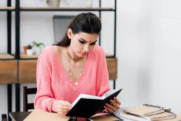 Indian student with bindi studying with notebooks and reading book at home — Stock Photo