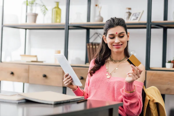 Mujer india sonriente con bindi sosteniendo tableta y tarjeta de crédito - foto de stock