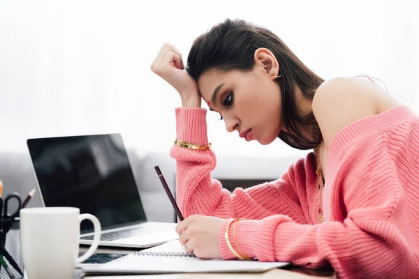 Schöne indische Frau lernt und schreibt in Notizbuch am Tisch mit Laptop — Stockfoto