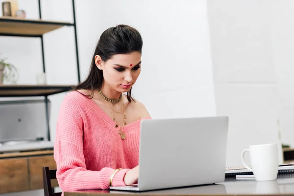 Attraente donna indiana con bindi utilizzando il computer portatile a tavola a casa — Foto stock