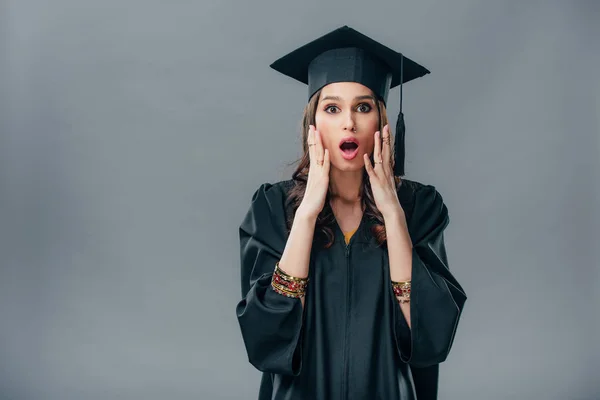 Estudante indiana chocado em vestido acadêmico e boné de formatura, isolado em cinza — Fotografia de Stock