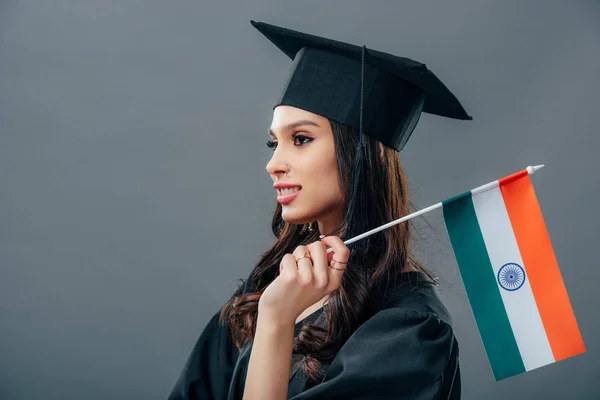 Étudiant indien en robe académique et casquette de graduation debout avec drapeau indien, isolé sur gris — Photo de stock