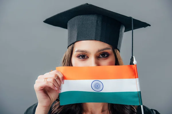 Индианка в шапке выпускника с индийским флагом, изолированная на сером — стоковое фото