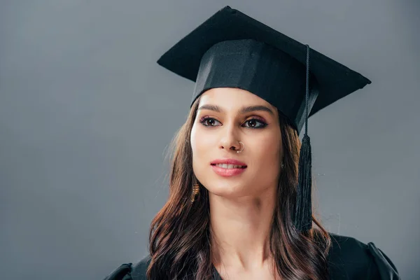 Elegante mujer india estudiante en sombrero de graduación, aislado en gris - foto de stock