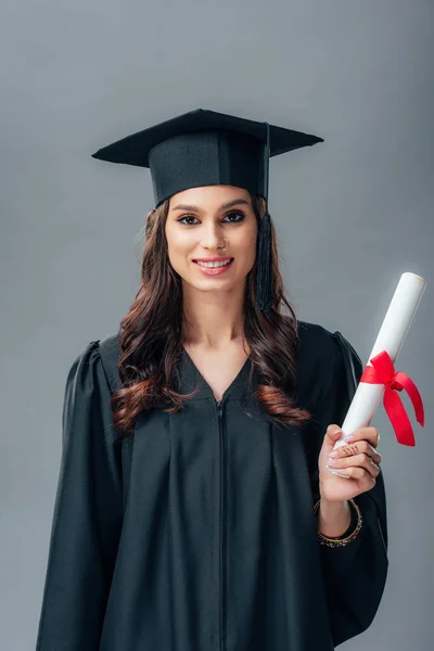 Sorridente studentessa indiana in abito accademico e cappello di laurea in possesso di diploma, isolata su grigio — Foto stock