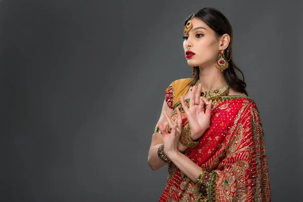 Приваблива індійська жінка в традиційному одязі, що показує гіанську мутру, ізольована на сірому — стокове фото