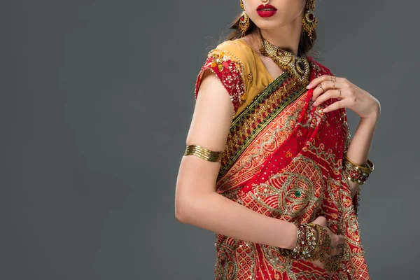 Обрезанный вид индийской женщины, позирующей в традиционных сари и аксессуарах, изолированных на сером — стоковое фото