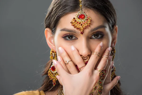 Atractiva mujer india con la cara de cierre bindi con las manos, aislado en gris - foto de stock