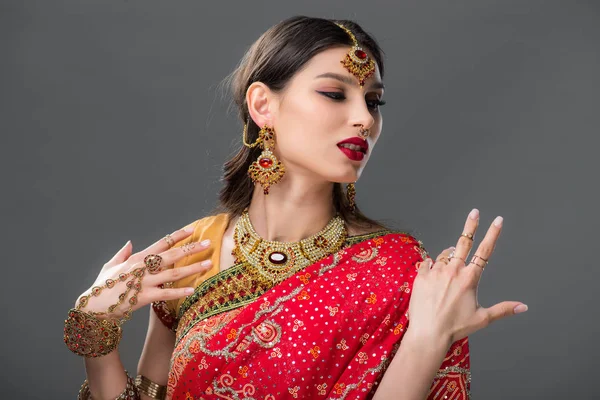 Atractiva mujer india haciendo gestos en sari tradicional, aislado en gris - foto de stock