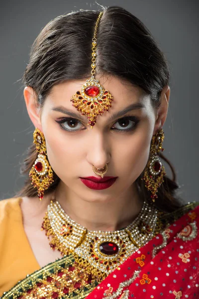 Привлекательная индийская девушка, позирующая в традиционном сари и аксессуарах, изолированная на сером — стоковое фото