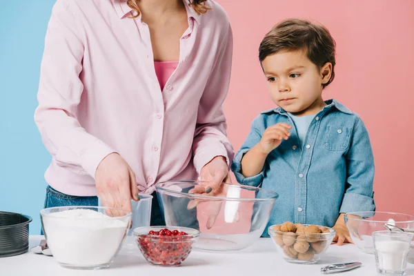 Милый маленький мальчик с матерью готовит ингредиенты для выпечки на двухцветном фоне — стоковое фото