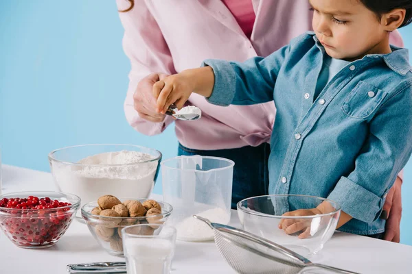 Little boy with mother pouring flour into measuring cup isolated on blue — Stock Photo