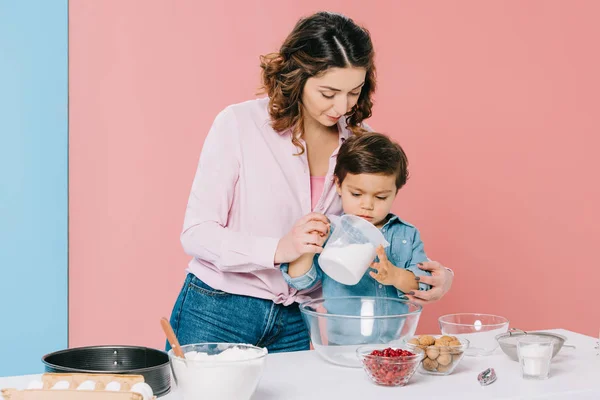 Little boy attentively looking at measuring cup in mothers hands on bicolor background — Stock Photo
