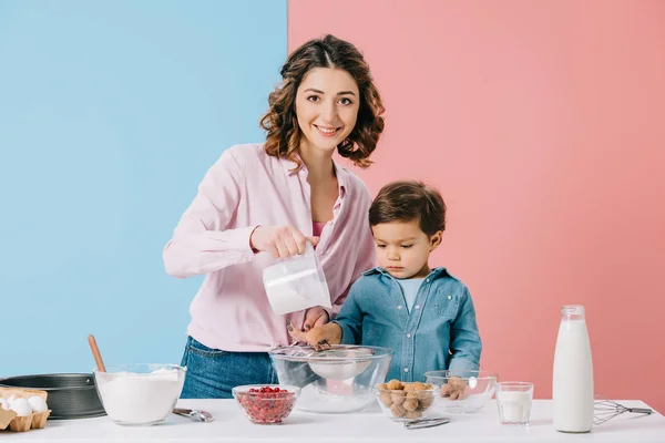 Mãe feliz cozinhar com o filho pequeno e olhando para a câmera no fundo bicolor — Fotografia de Stock