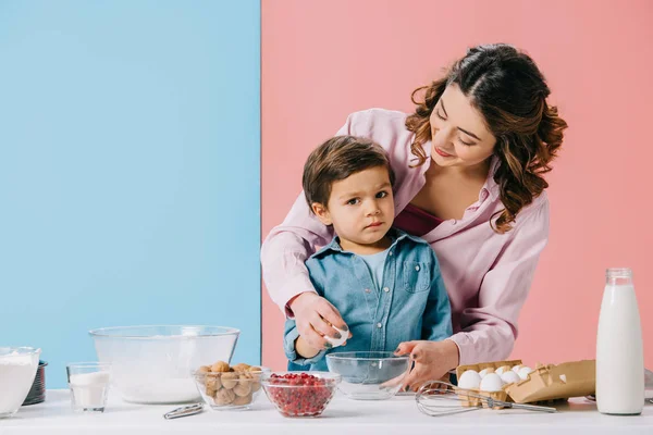 Feliz mamá abrazando pequeño hijo sosteniendo huevo sobre fondo bicolor - foto de stock