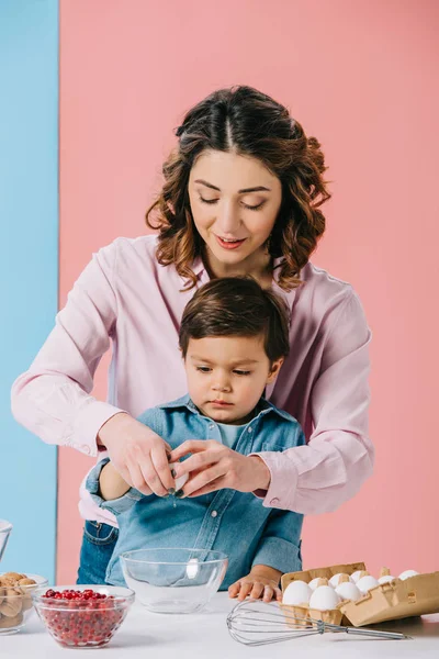 Mère avec petit fils casser oeuf ensemble sur fond bicolore — Photo de stock