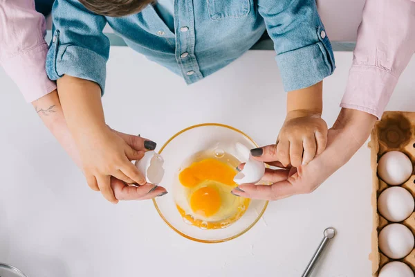 Vue partielle de la mère et du fils cassant l'oeuf dans un bol ensemble sur fond blanc — Photo de stock