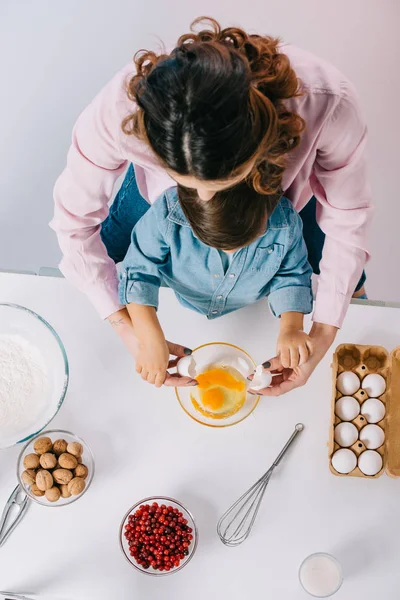 Madre e piccolo figlio cucinare insieme e rompere le uova a ciotola su sfondo chiaro — Foto stock