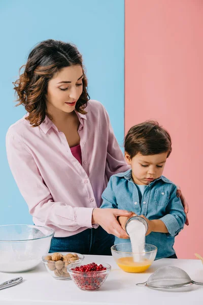 Mother helping little son adding sugar to whipped eggs on bicolor background — Stock Photo