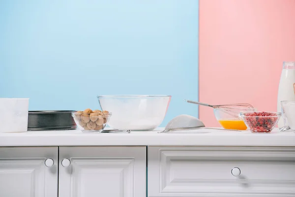 Diferentes produtos e utensílios de cozinha na mesa de cozinha branca no fundo bicolor — Fotografia de Stock