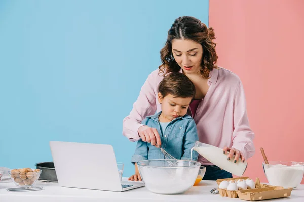 Lindo niño mirando a la pantalla del ordenador portátil, mientras que la madre agrietamiento de nogal sobre fondo bicolor - foto de stock