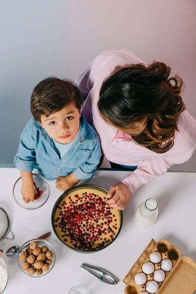 Top view of cute little boy with mother adding cranberries to baking form isolated on pink — Stock Photo