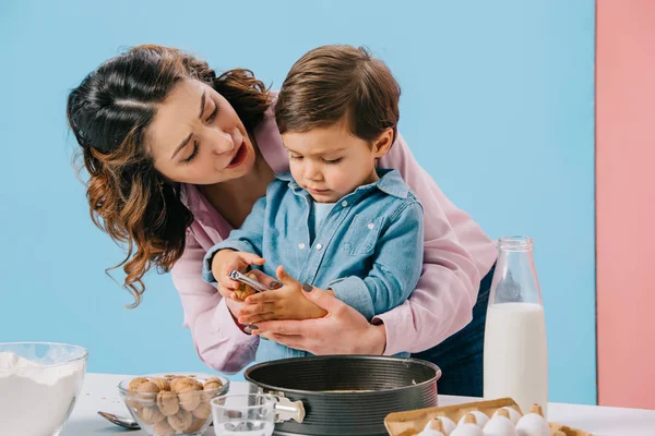 Мать обнимает милого маленького сына, разбивая грецкие орехи на двухцветном фоне — стоковое фото