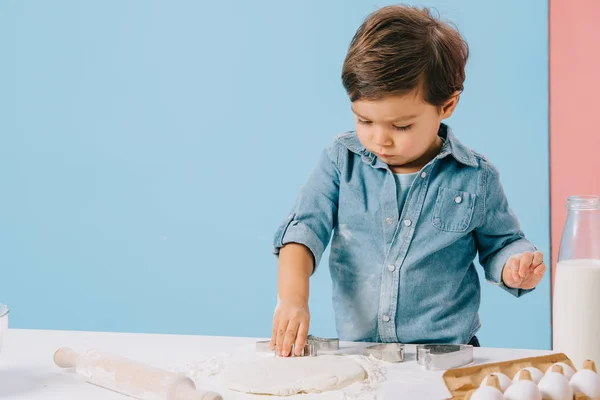 Niedlicher kleiner Junge schneidet fleißig Figuren in Teig mit Teigformen auf zweifarbigem Hintergrund — Stockfoto