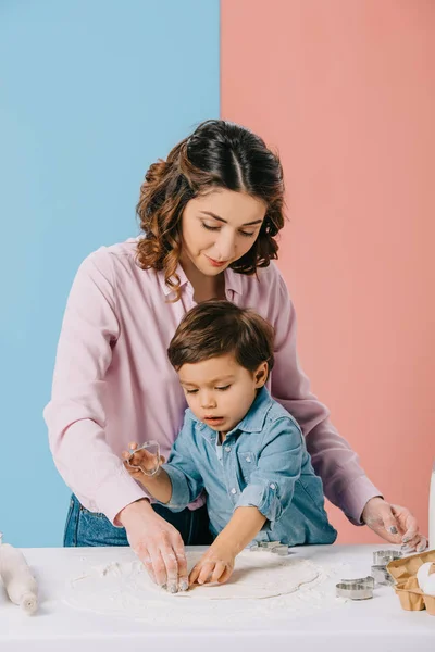 Mutter mit kleinem Sohn schneidet gemeinsam Figuren in Teig auf zweifarbigem Hintergrund — Stockfoto