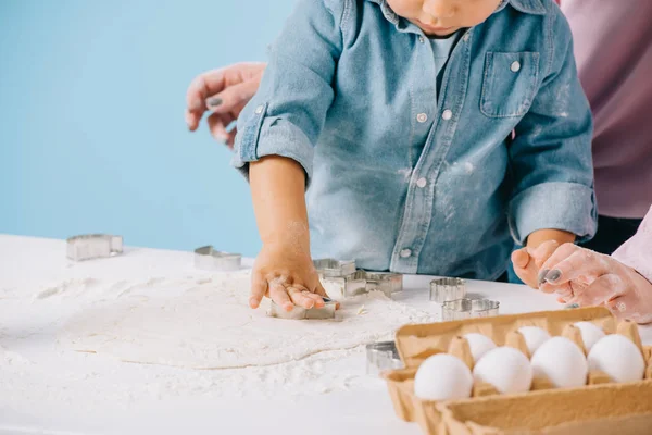Cropped view of cute little boy cutting figures in dough together with mother isolated on blue — Stock Photo