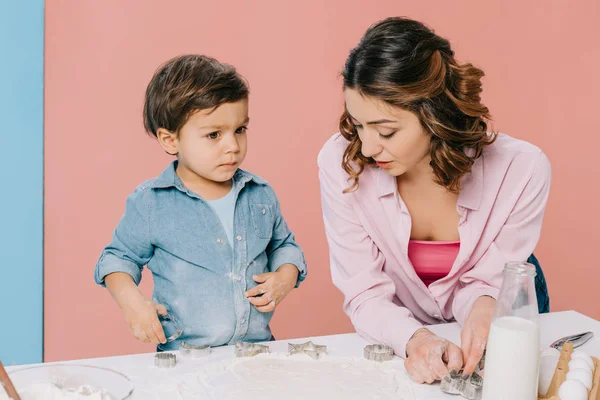 Madre con simpatico piccolo figlio cottura pasticceria insieme a tavolo da cucina bianco su sfondo bicolore — Foto stock