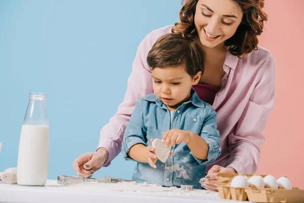 Glückliche Mutter mit niedlichem kleinen Sohn, der gemeinsam Kekse auf zweifarbigem Hintergrund backt — Stockfoto